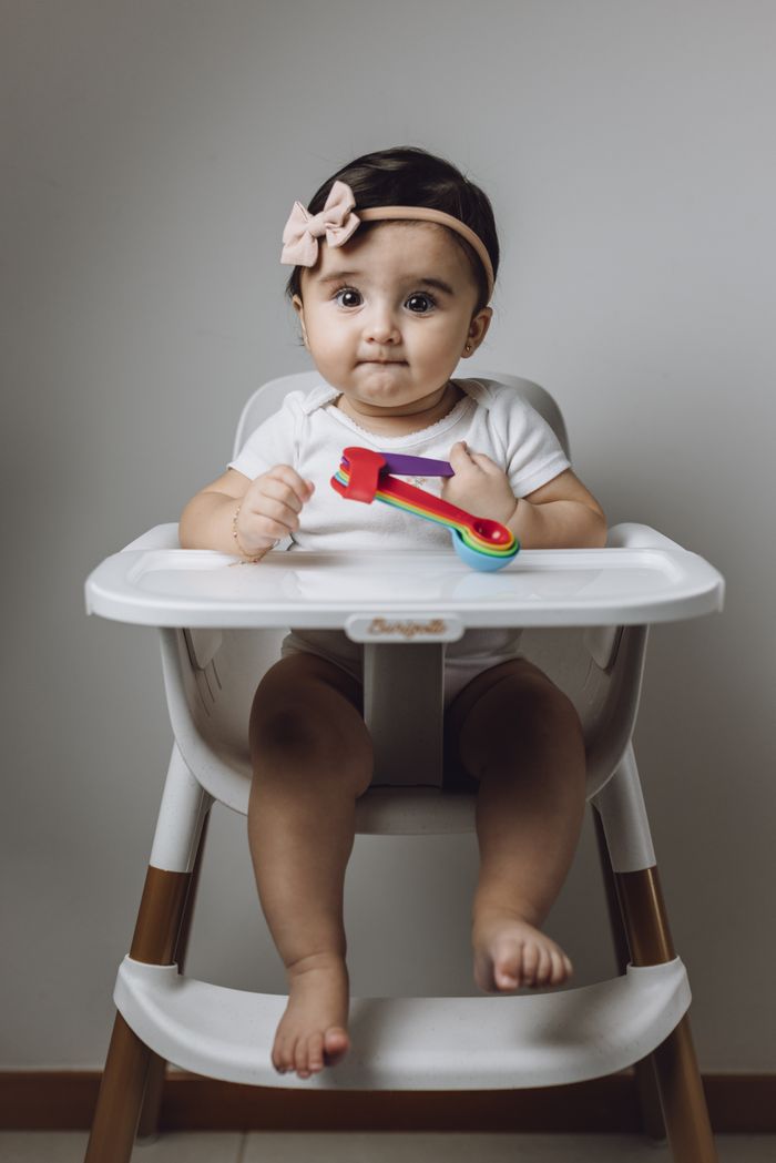Cute baby girl with colorful toy sitting in high chair. Perfect for childcare themes.