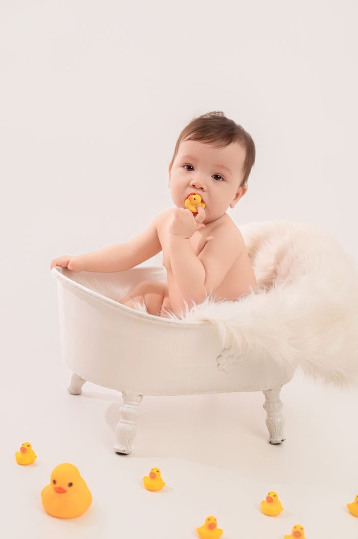 Charming baby playing with rubber ducks in a small bathtub setting.