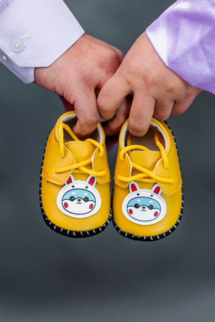 Vibrant yellow baby shoes with cute cartoon designs held by two adults' hands.