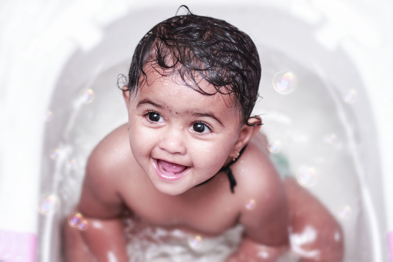 Adorable baby enjoying a bath with bubbles, showcasing a joyful smile and playful expression.