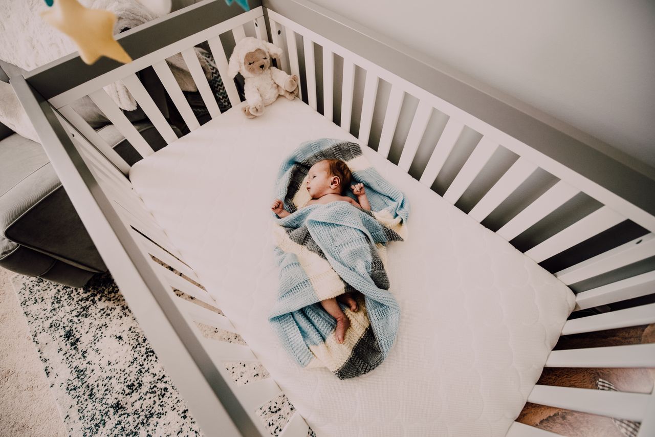 A peaceful baby wrapped in a blanket sleeps in a cozy crib, creating a serene nursery atmosphere.